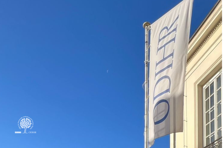 Flag with "ODIHR" text on a building against a clear blue sky.