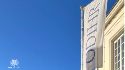 Flag with "ODIHR" text on a building against a clear blue sky.
