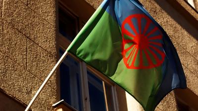 Romani flag with blue and green halves, red spoked wheel, waving on a building.