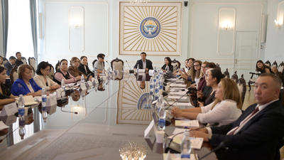 People sitting around a large conference table in a formal meeting room with chandeliers.