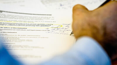 Hand writing notes on printed documents with text and highlights.