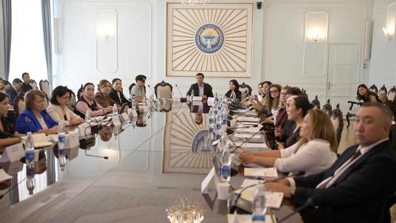 People sitting around a large conference table in a formal meeting room with chandeliers.