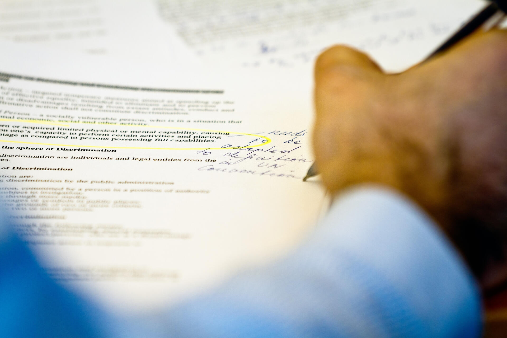 Hand writing notes on printed documents with text and highlights.